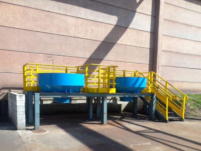 Silos para moega instalados em estrutura metálica elevada, com acesso por escada e plataforma com guarda-corpo, na obra da MetalPinda.