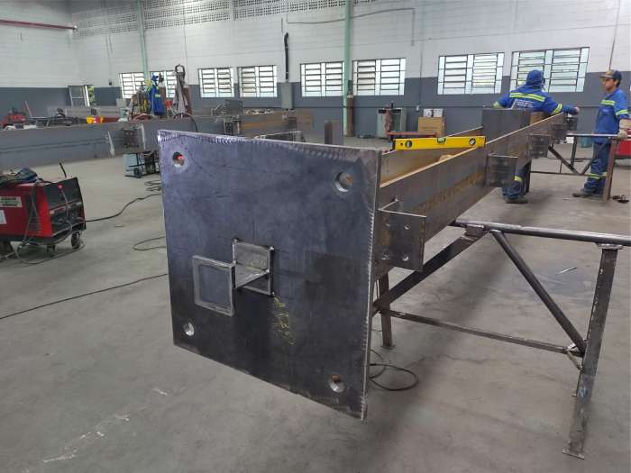 Detalhe da extremidade de viga metálica com furações e suporte soldado, parte de estrutura industrial em fabricação na MetalPinda.