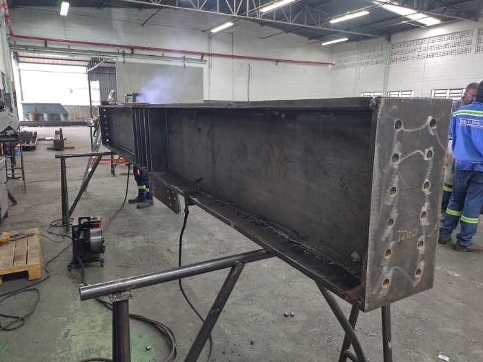 Soldagem de viga metálica de grande porte para estrutura industrial, com acabamento lateral perfurado, no galpão da MetalPinda.