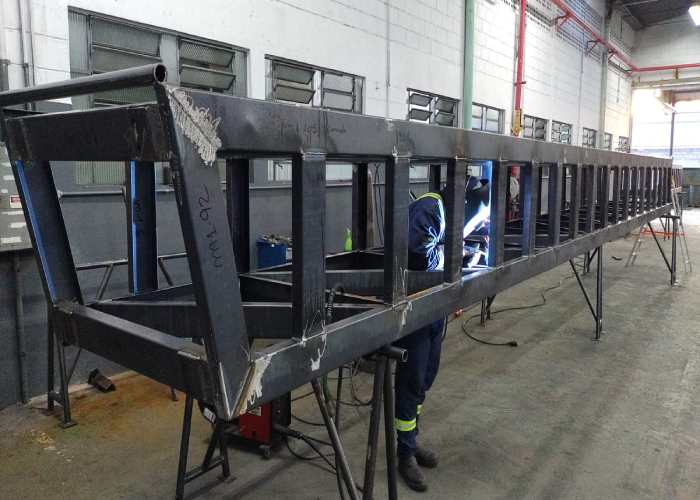Soldador realizando montagem e soldagem de estrutura metálica de grande porte para silo de moega, no galpão da MetalPinda.